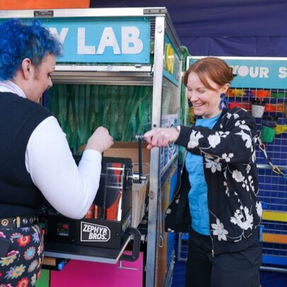 A person with blue hair at a vending machine as another person directs them on how to use it. 