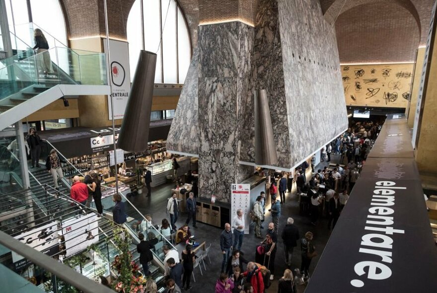 View from first floor into a Mercato Centrale in an Italian city, showing people shopping and eating in the artisanal food hall on the ground floor.