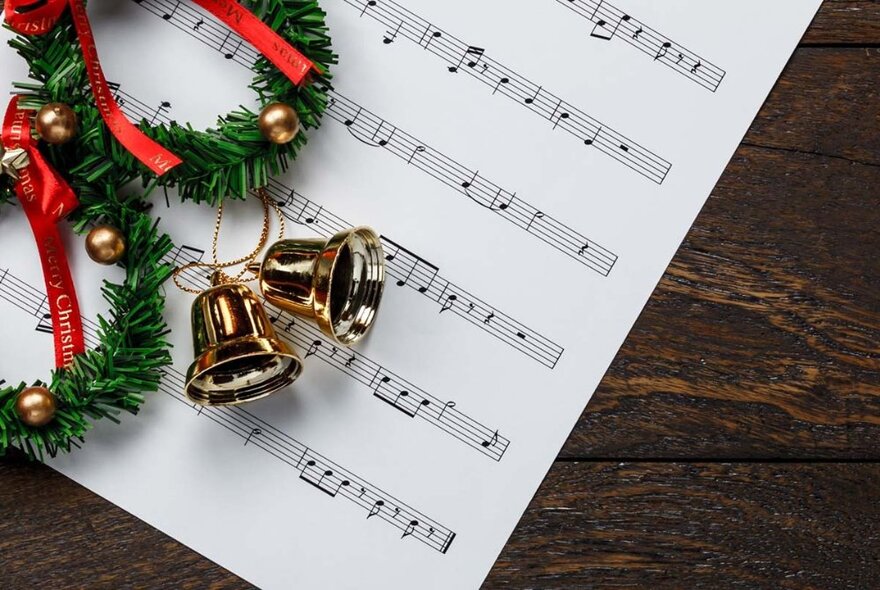 Sheet of music lying on a wooden table with holly wreathes and bells.