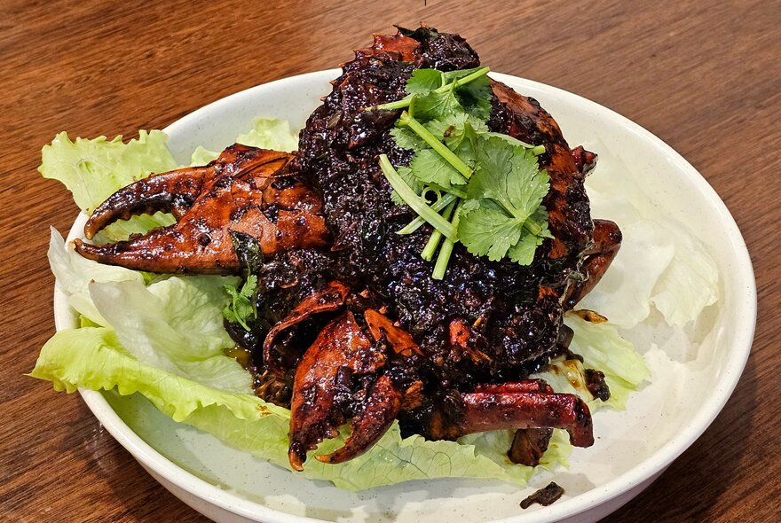 A Malaysian fried crab on a bed of lettuce in a bowl, with a green leafy garnish on top.
