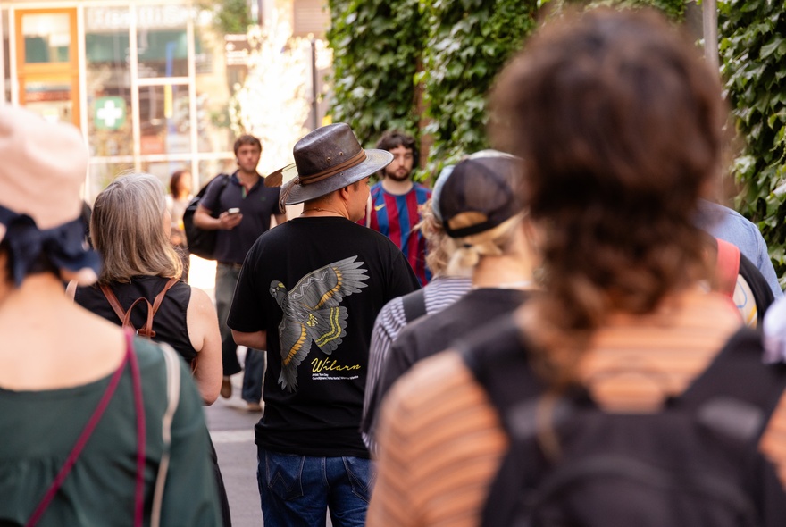 People listening to a speaker outside, with his back to the crowd.