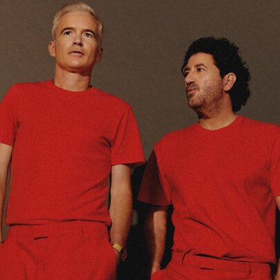 Australian electronic music group The Avalanches, two middle-aged men wearing matching red outfits, posed against a light brown backdrop.