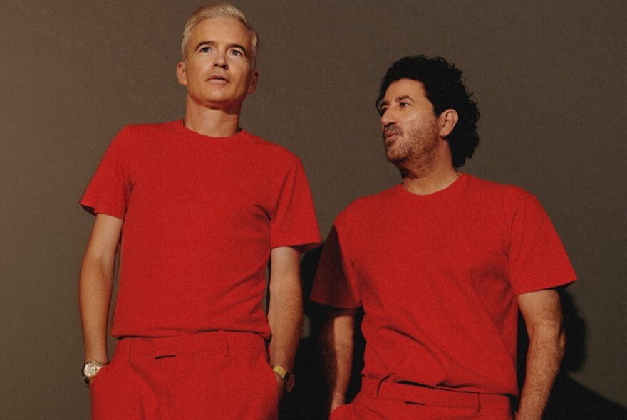 Australian electronic music group The Avalanches, two middle-aged men wearing matching red outfits, posed against a light brown backdrop.