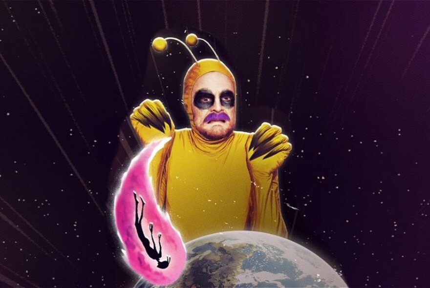 A man with a ginger moustache dressed as an  alien with bobbled antennae, near a model of Earth with a pink comet flying in. 