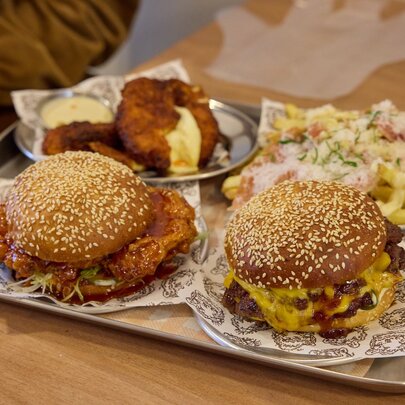 A tray with two burgers in sesame seed buns with chicken poking out and sauce oozing down, loaded fries and patties. 