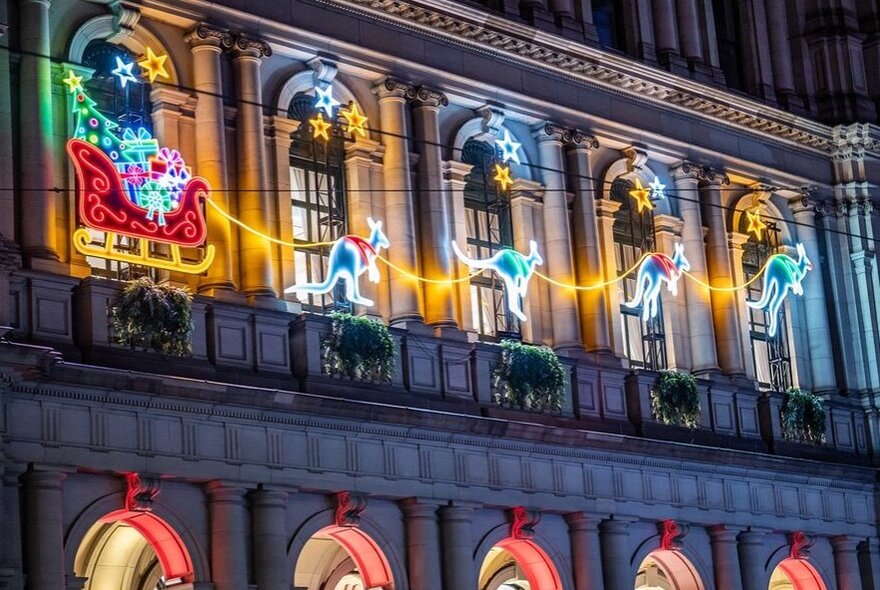 A neon light Santa on his sleigh led by kangaroos, displayed on the side of a building.