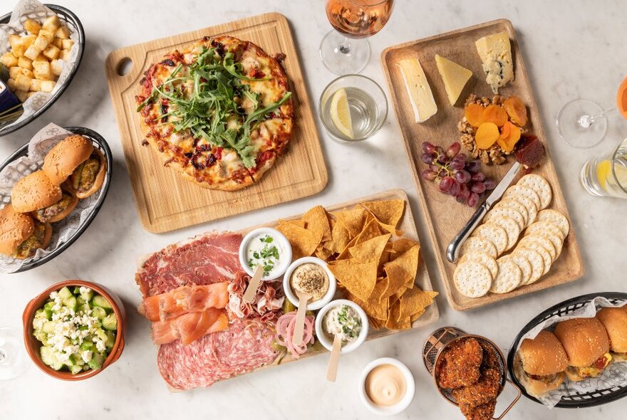 A table filled with food including fried chicken, pizza, sliders, charcuterie and a cheese board.