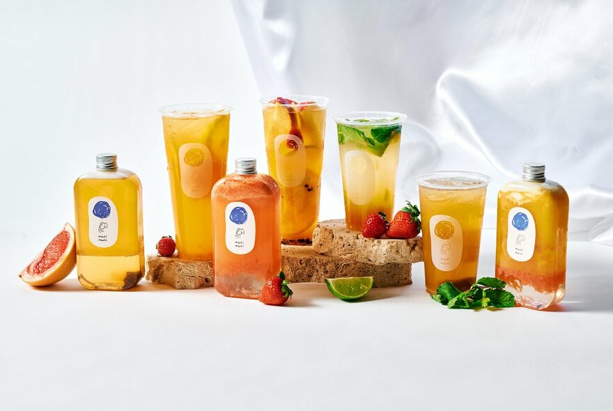 A selection of bubble teas presented on a white surface with pieces of fruit.