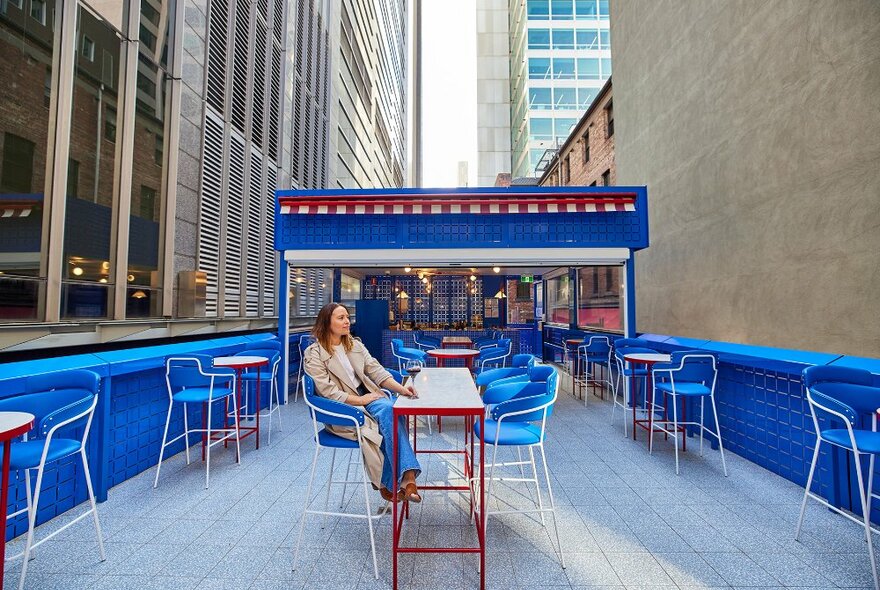 A woman sitting on a bright blue and red rooftop with a glass of wine.