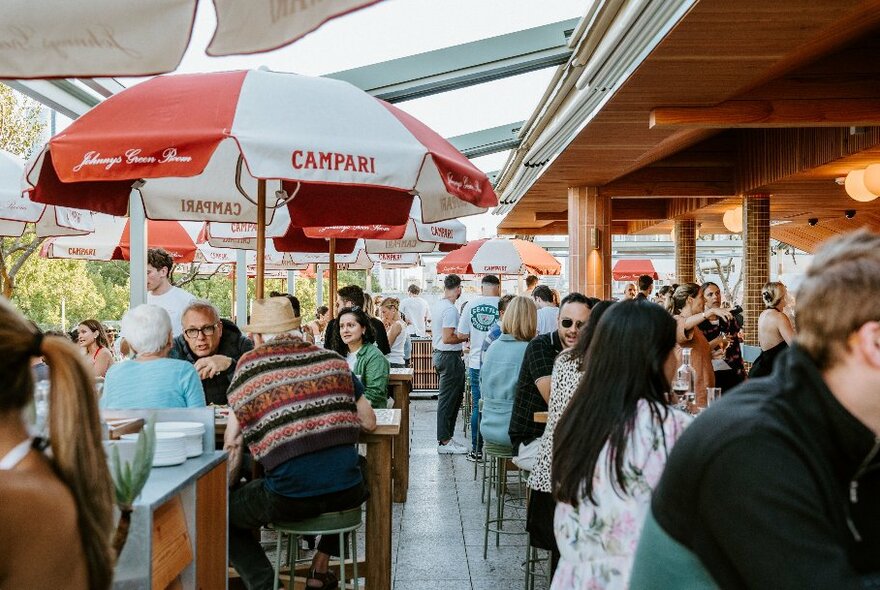 Open air rooftop bar with patrons sitting at high tables under shade umbrellas.