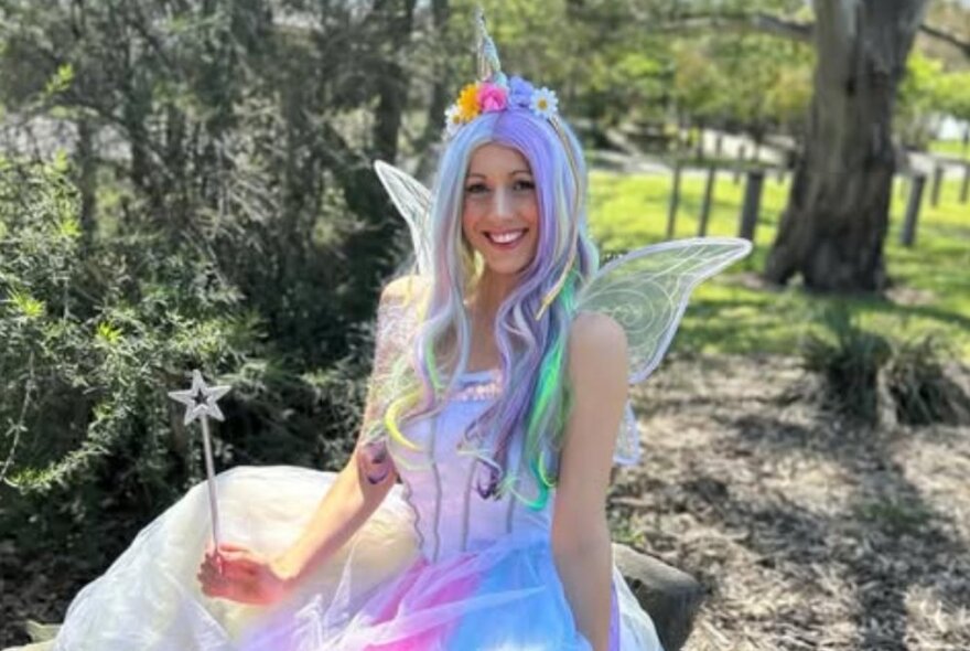 WOman dressed as a fairy holding a star-shaped wand and wearing a unicorn headdress.