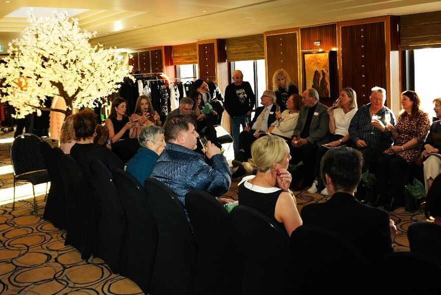 People sitting in a small room with patterned carpet and an illuminated tree. 