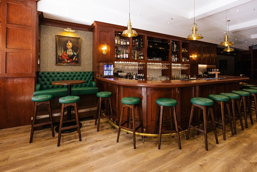 A classic English pub decor with a wooden bar and green bar stools. 