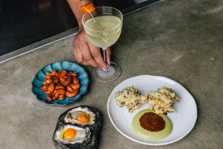 A selection of food including fried cauliflower and oyster shells with raw eggs displayed on a concrete surface.