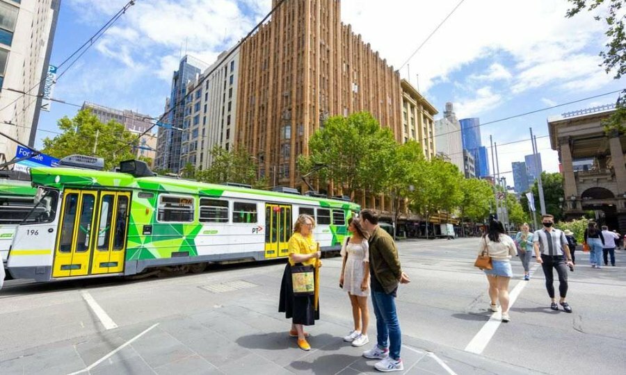 Three people standing on a street corner as a tram passes by