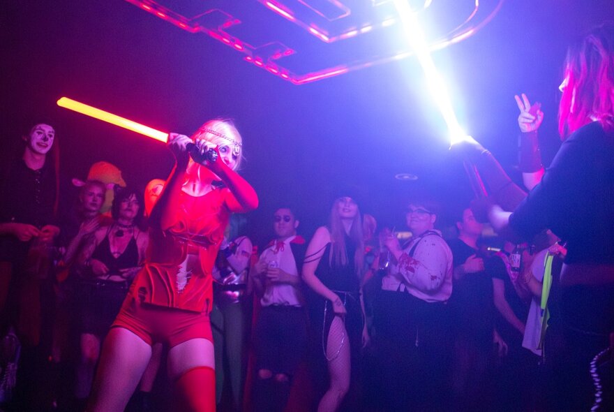 Person with light sabre in a crowded purple-lit nightclub.