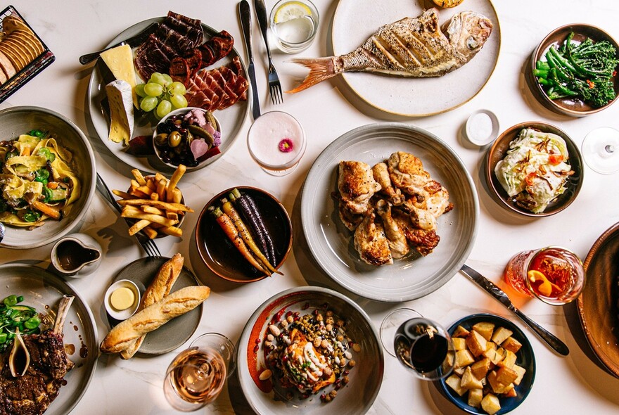 Plates of food including a whole fish, meat, bread rolls and roasted vegetables.