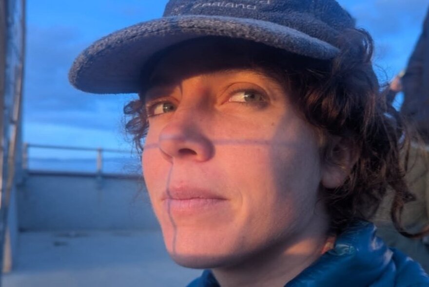 Illustrator and comic artist Sofia Sabbagh, her face close up to the viewer, wearing a cap and  smiling slightly, posed outdoors in dusk light.