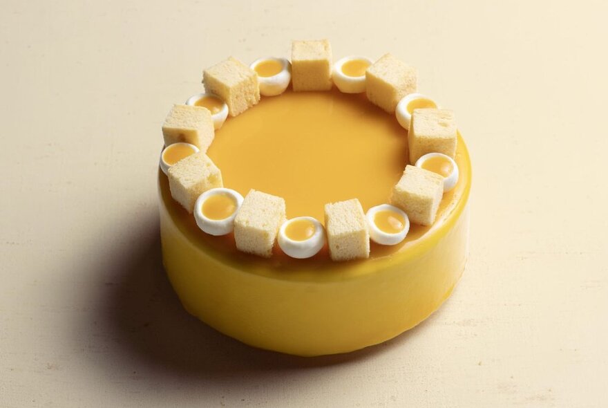 A yellow cheesecake garnished with chiffon sponge cubes and yoghurt mousse paired with mango coulis.