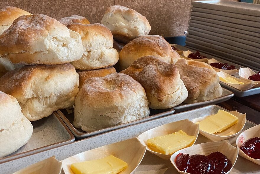 A tray of scones alongside small bowls of butter and jam.