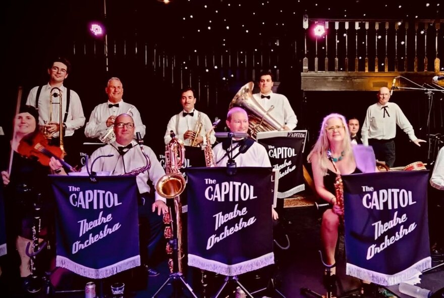 The Capitol Theatre Orchestra performing on stage with their branded purple music stands