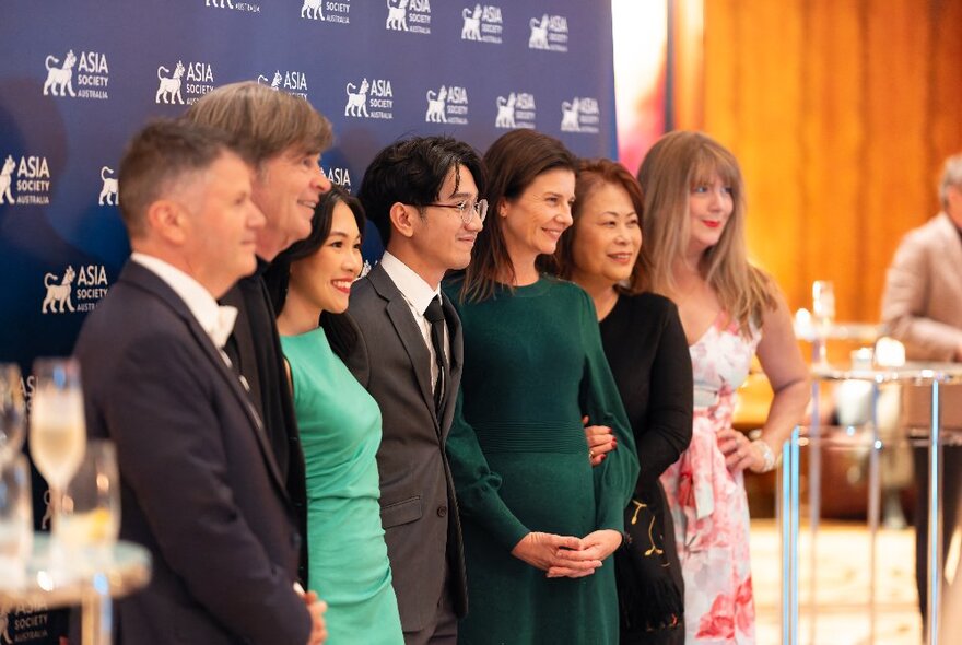 People lined up in front of a branded screen having their photograph taken as a group.