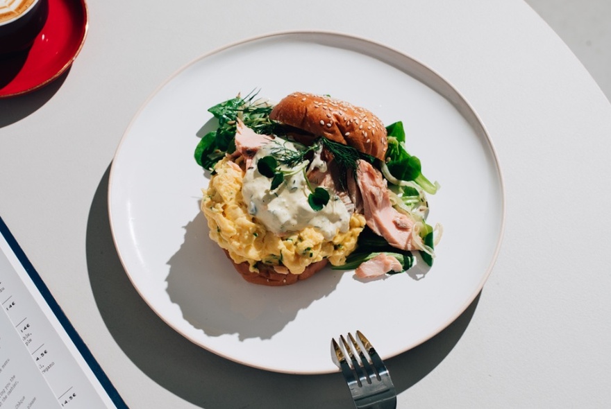 A round white plate of scrambled eggs served on a brioche with a fork.