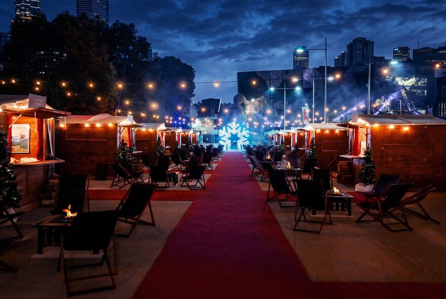 An outdoor alpine village pop-up event at Fed Square at night, featuring private wooden chalets, string lights, and a red carpet.