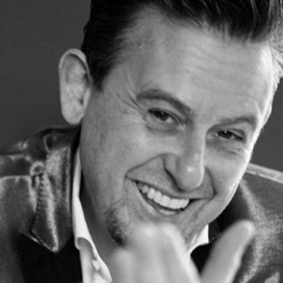 Musician smiling, his hand towards the camera, wearing a shiny suit.