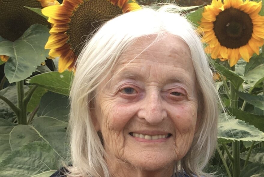 A portrait of author, Lorna Hannan, in front of two sunflowers.