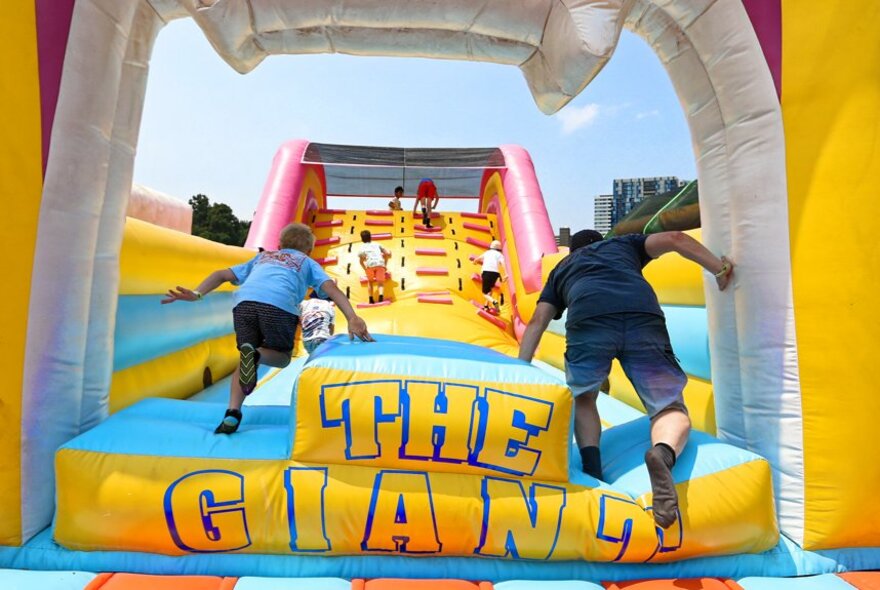 Two people at the entrance to a giant inflatable slide attempting to run up it to reach the top.