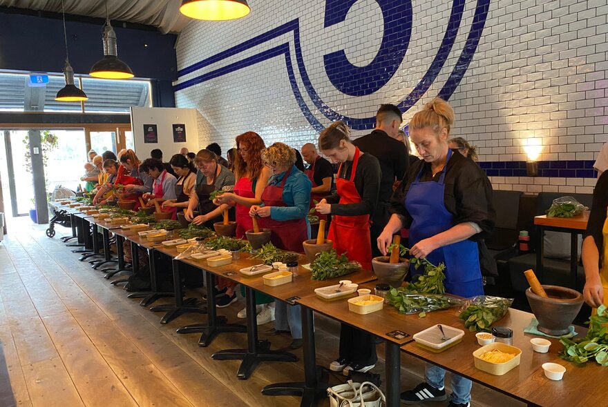A group of people wearing aprons and standing behind a long wooden table as they participate in an Italian cooking class.