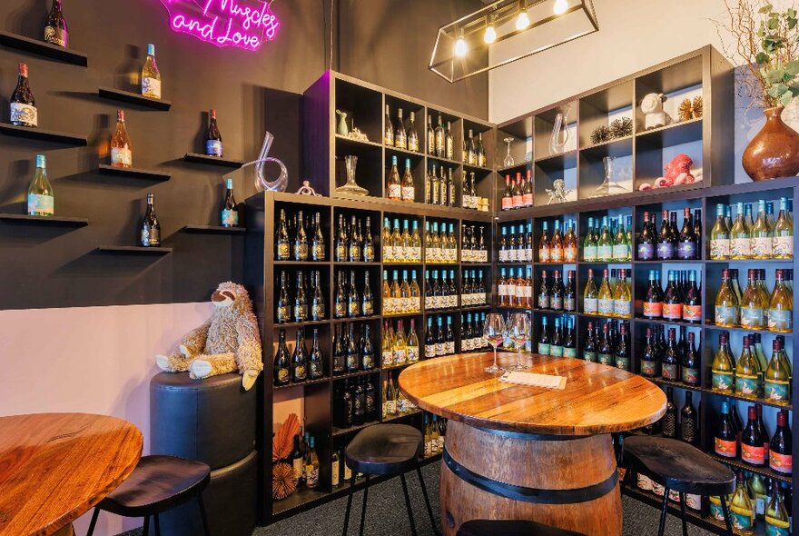 Wine bar interior with stacked shelves of wine, round tables on wine barrels with stools.