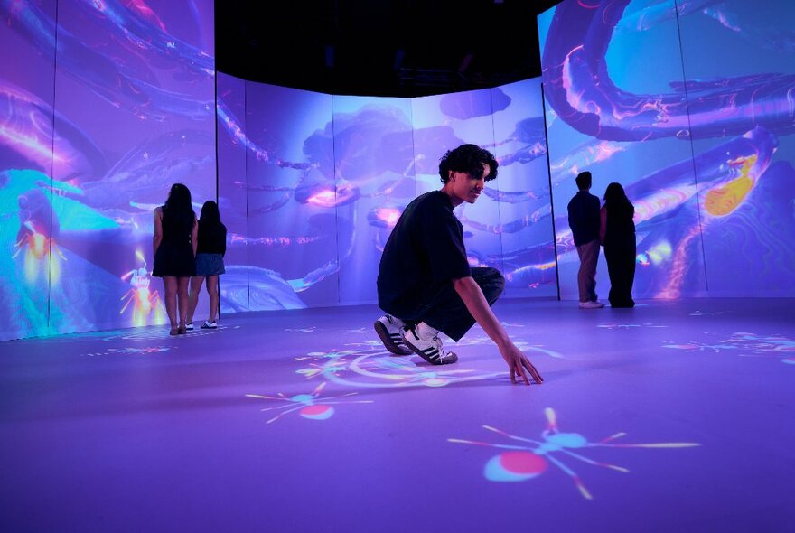 People looking at giant projections on the walls and floor in a room with screens, the images are swirly and blue and purple tones. 