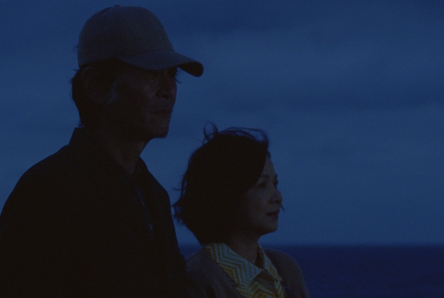 A dark silhouette of two people looking out into the distance as night falls.