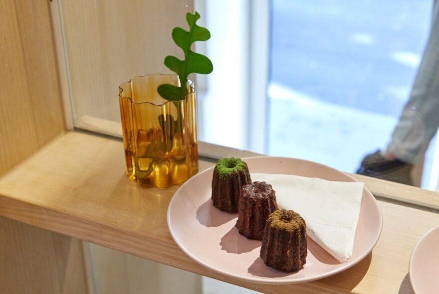 Wooden shelf with pink plate holding three caneles