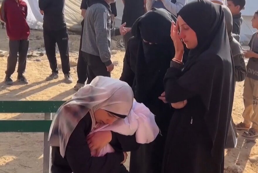 Women wearing hijabs weeping and covering their faces.