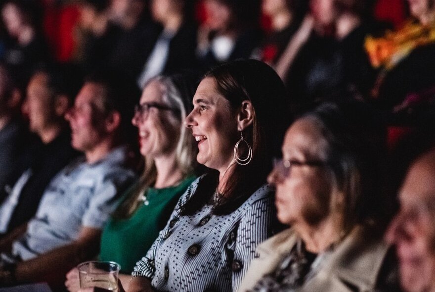 Seated audience in a dark venue, looking ahead at a screen.