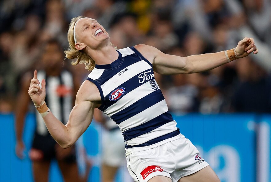 A Geelong AFL football player on the field during a match, celebrating a goal.