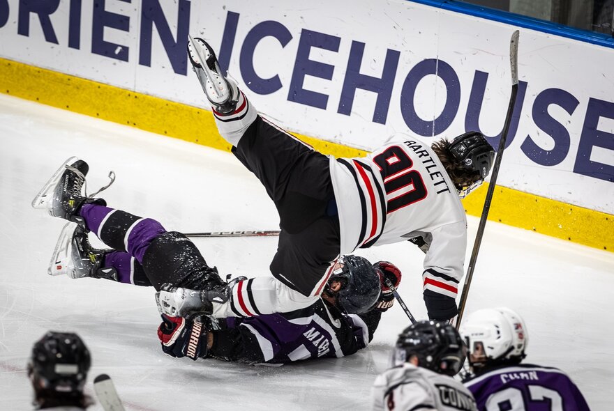 Two ice hockey players falling on the ice during a game.