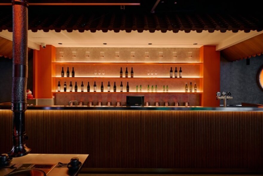 Low-lit bar with shelves and moody lighting in a restaurant setting.