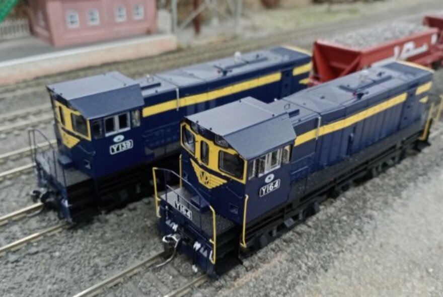 Two blue model trains on separate tracks, one pulling rocks or gravel in a freight carriage.