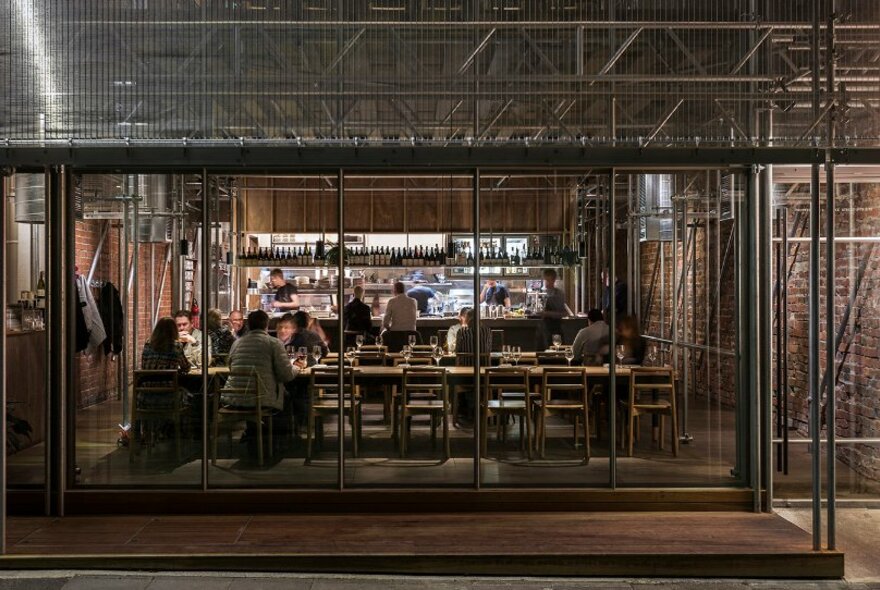 Street view of exterior of Sunda restaurant showing diners seated at tables inside and kitchen in background.