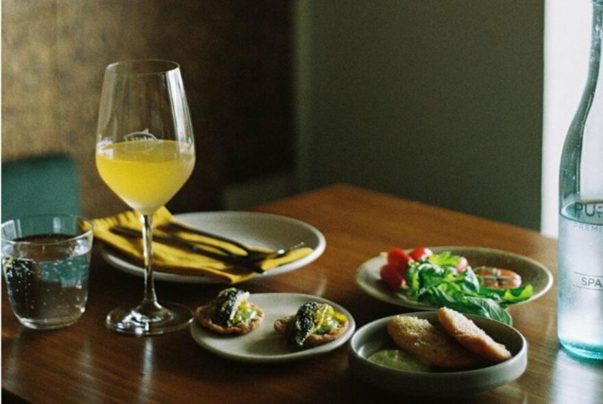 Restaurant dining table set with a yellow cocktail and three small dishes of savoury food.