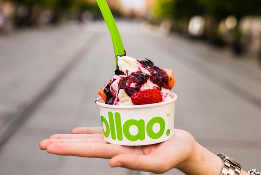 White cup with lime green wording and spoon inserted into yoghurt and fruit, on outstretched hand.