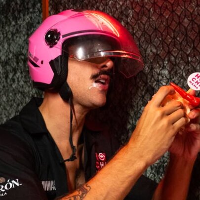 Man wearing a crash helmet biting into a katsu sandwich.