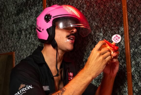 Man wearing a crash helmet biting into a katsu sandwich.