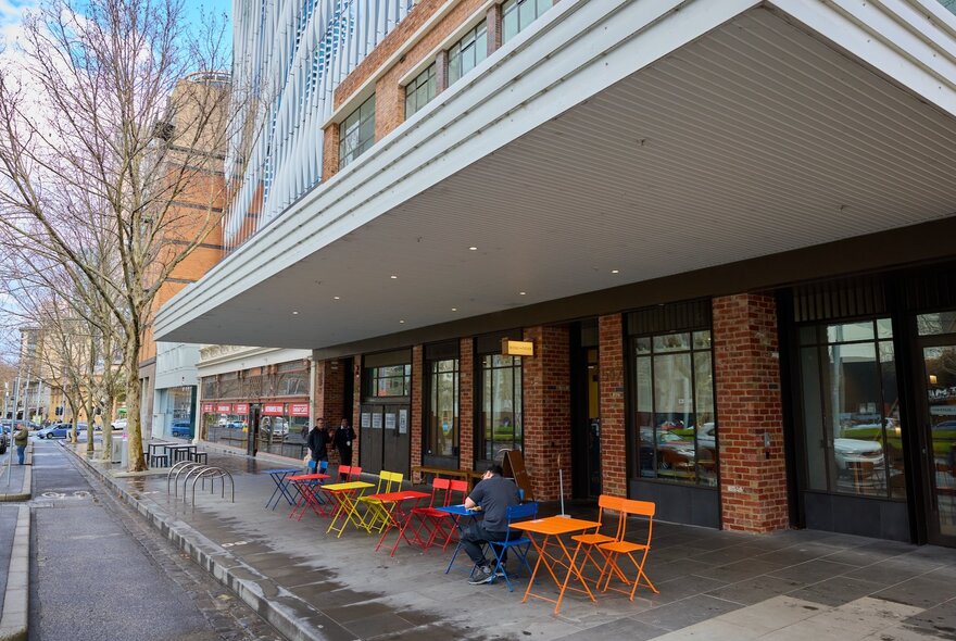 The exterior of Seoul Tiger 1988 with coloured chairs and tables and a single person eating outside. 