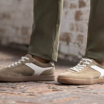 Men's feet wearing a pair of suede casual sneakers, and khaki straight-legged pants.