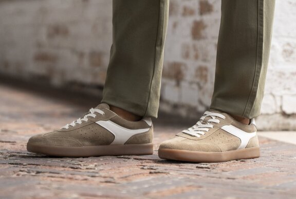Men's feet wearing a pair of suede casual sneakers, and khaki straight-legged pants.